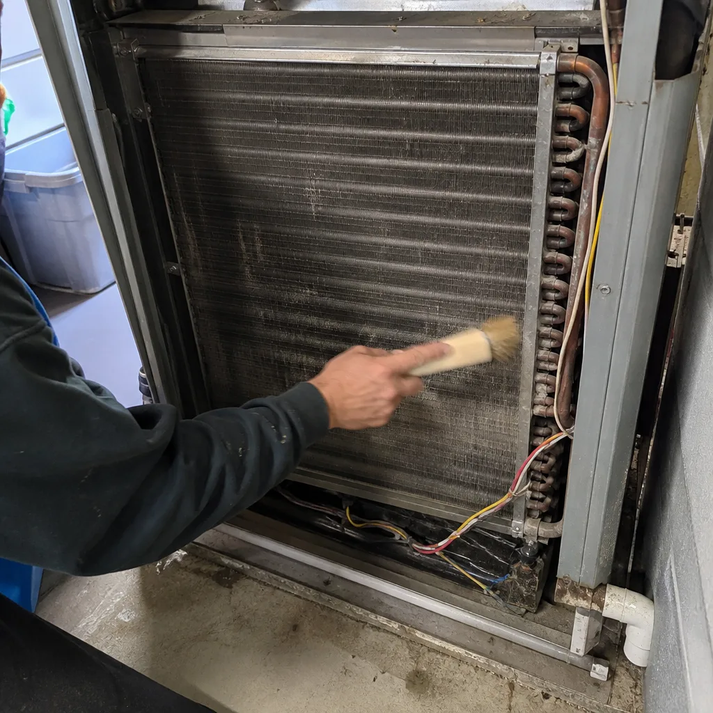 HVAC technician cleaning dusty evaporator coil fins with a brush